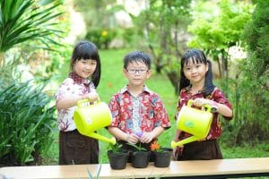 Three children enjoying gardening in a lush green garden with watering cans.