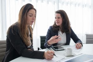 Two women in a business meeting discussing ideas while taking notes.