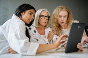 Diverse group of women across generations engaging with a tablet indoors.